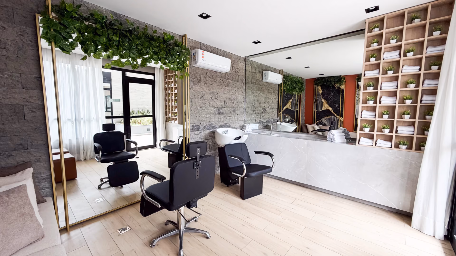 Beauty care com duas cadeiras de cabeleireiro, lavatório, bancada de pedra, estante com toalhas e espelho com plantas pendentes